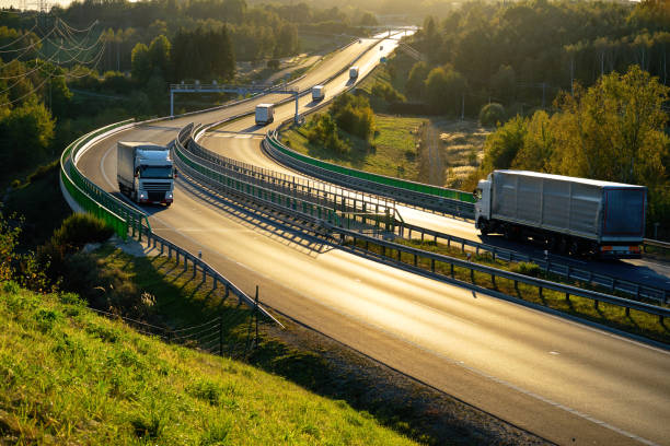 white trucks passing through tollgates on the highway in backlit - convoy imagens e fotografias de stock