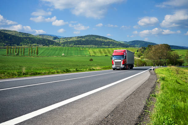 istock Red truck arriving on the asphalt road between green fields 648258550