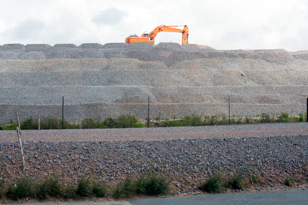 An excavator is loading on top of a mountain of stone material at a road building project.