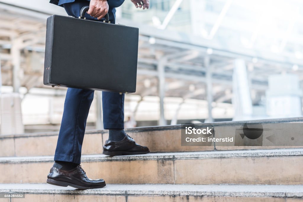 businessman holding leather briefcase while walking Close up shot of businessman holding leather briefcase while walking upward on the stair outdoor in city. Briefcase Stock Photo