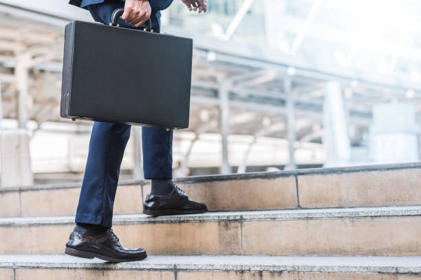 businessman holding leather briefcase while walking Close up shot of businessman holding leather briefcase while walking upward on the stair outdoor in city. power walking photos stock pictures, royalty-free photos & images