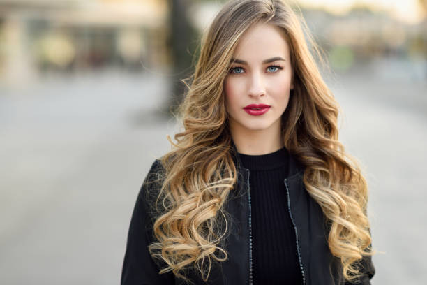 Young blonde girl with beautiful blue eyes wearing black jacket. Close-up portrait of young blonde girl with beautiful blue eyes wearing black jacket outdoors. Pretty russian female with long wavy hair hairstyle. Woman in urban background. long hair stock pictures, royalty-free photos & images
