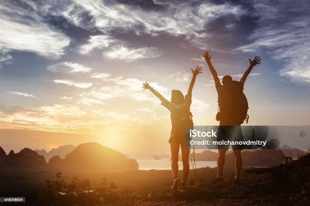 Happy couple winner success concept mountains Happy couple stands in winner pose with rised arms on background of sunrise mountains and sea. Success concept Couple - Relationship Stock Photo