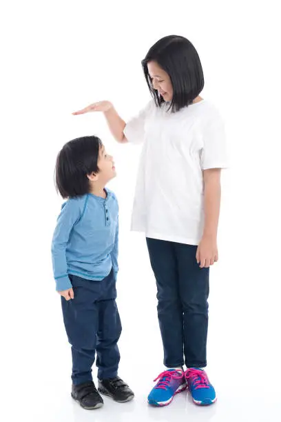 Asiangirl measures the growth of her brother on white background isolated