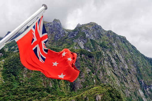 The New Zealand Red Ensign and the rugged mountains of the Milford Sound on the South Island of New Zealand