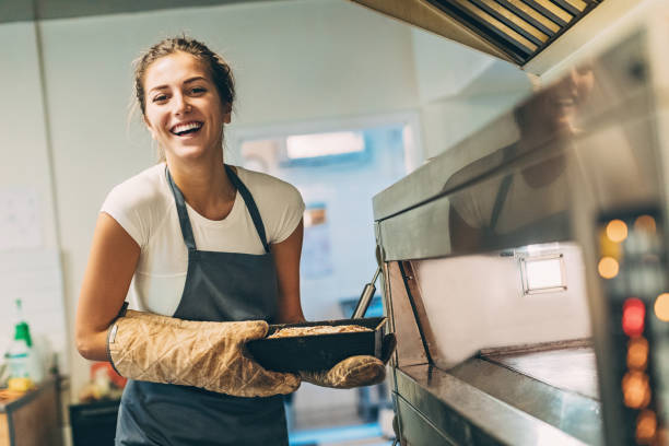 Beautiful baker holding hot bread Young baker taking the hot bread out of the stove baking bread stock pictures, royalty-free photos & images