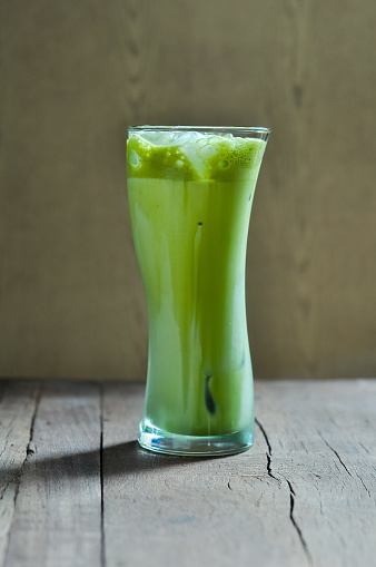 Iced matcha green tea latte in curve glass on wooden table