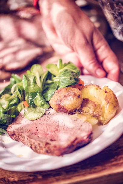 Eating medium roasted Roast Beef with crunchy potatoes, root vegetables and fresh salad for lunch.