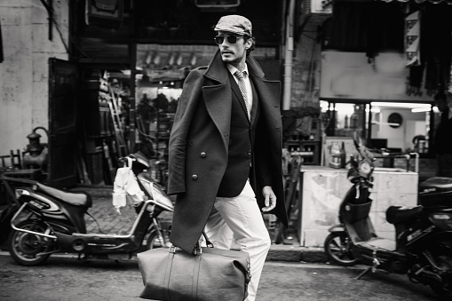 One man, outdoors in the city, cool and elegant, caries a leather bag, black and white photo.