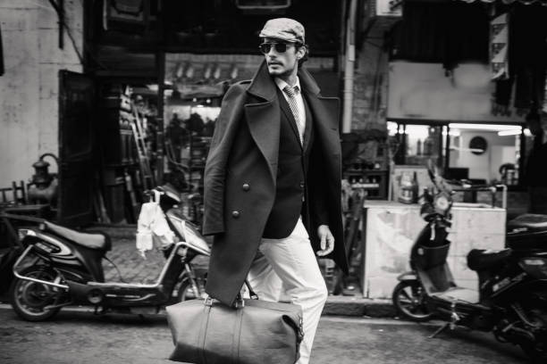 Handsome traveler One man, outdoors in the city, cool and elegant, caries a leather bag, black and white photo. preppy fashion stock pictures, royalty-free photos & images