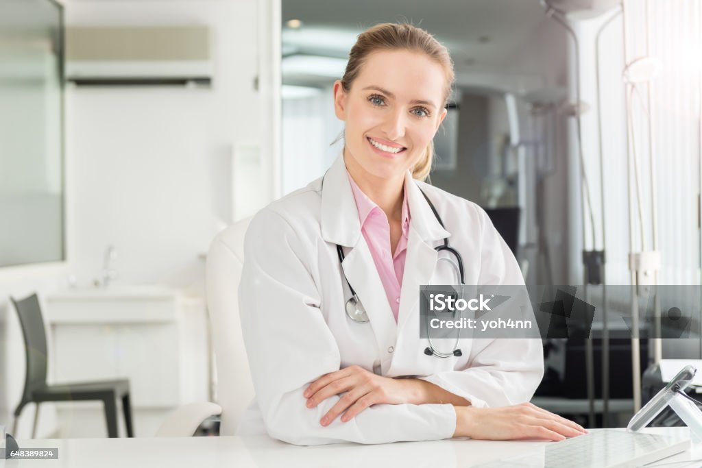 Beautiful medicine worker Horizontal color image of pretty female doctor at office sincerely smiling at camera. Wearing white lab coat and stethoscope around neck. Gynecologist Stock Photo