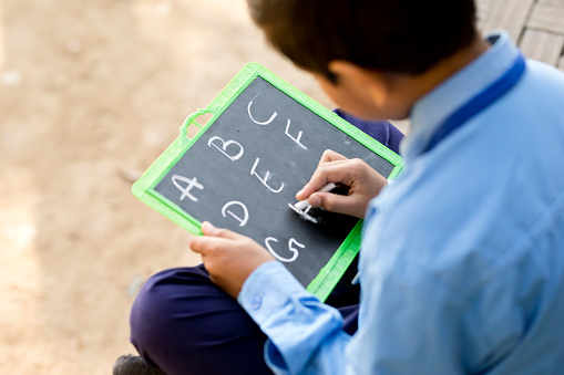 Little school boy in uniform writing on vintage school slate