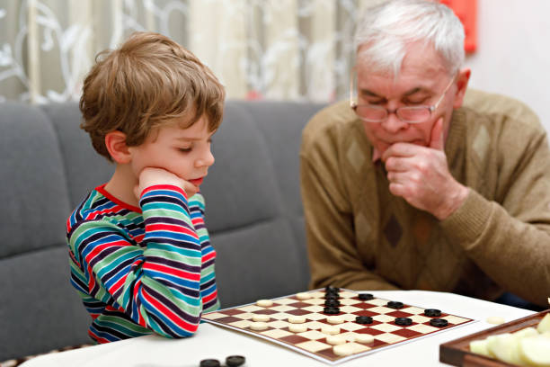 poco niño a niño y abuelo senior jugando juntos damas juego - concentration chess playing playful fotografías e imágenes de stock