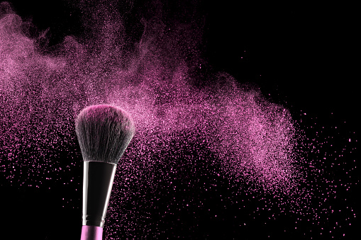 pink blush exploding over a cosmetic brush isolated on black background