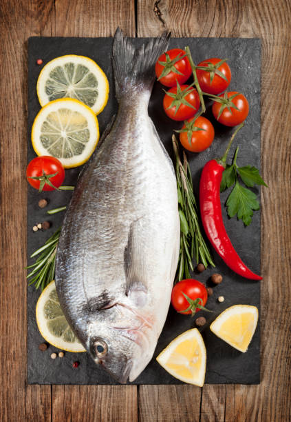 istock Fresh fish, lemon, spices and cherry tomatoes on a stone board 648445852