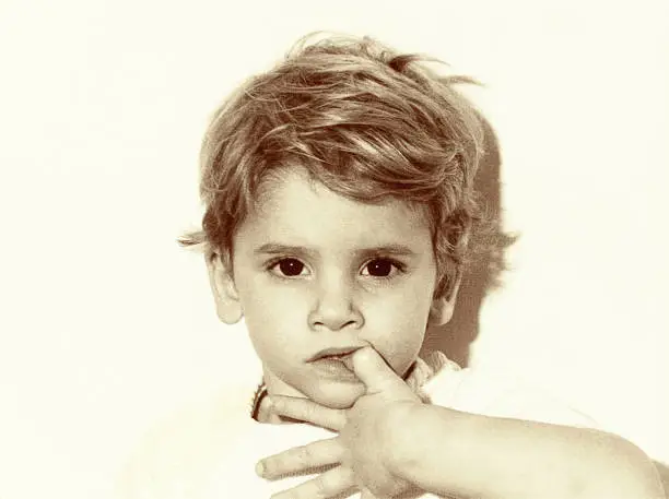 Vintage photo, grainy black and white of a close up kid biting nails with very serious face looking at camera.