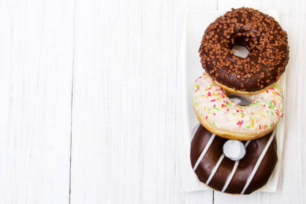 Tasty donuts with icing and chocolate on white wooden background