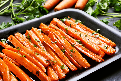 Fried carrots with green herbs in baking tray, close up