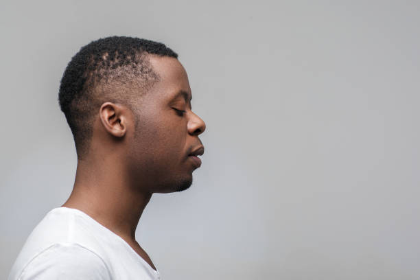 Concentrated black guy looking right. Profile view Concentrated african man with closed eyes on grey background with free space. Deep concentration, yoga, meditation. Profile view. african tribal culture photos stock pictures, royalty-free photos & images