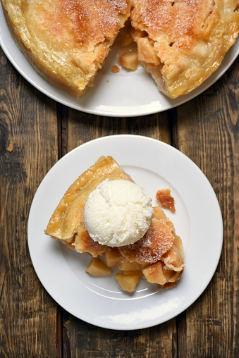 Piece of apple pie served with ice cream, fruit baking on wooden background, top view