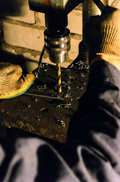 istock working in the workshop, which is on the drill press drill metal parts. He wore overalls and dirty gloves 648564486