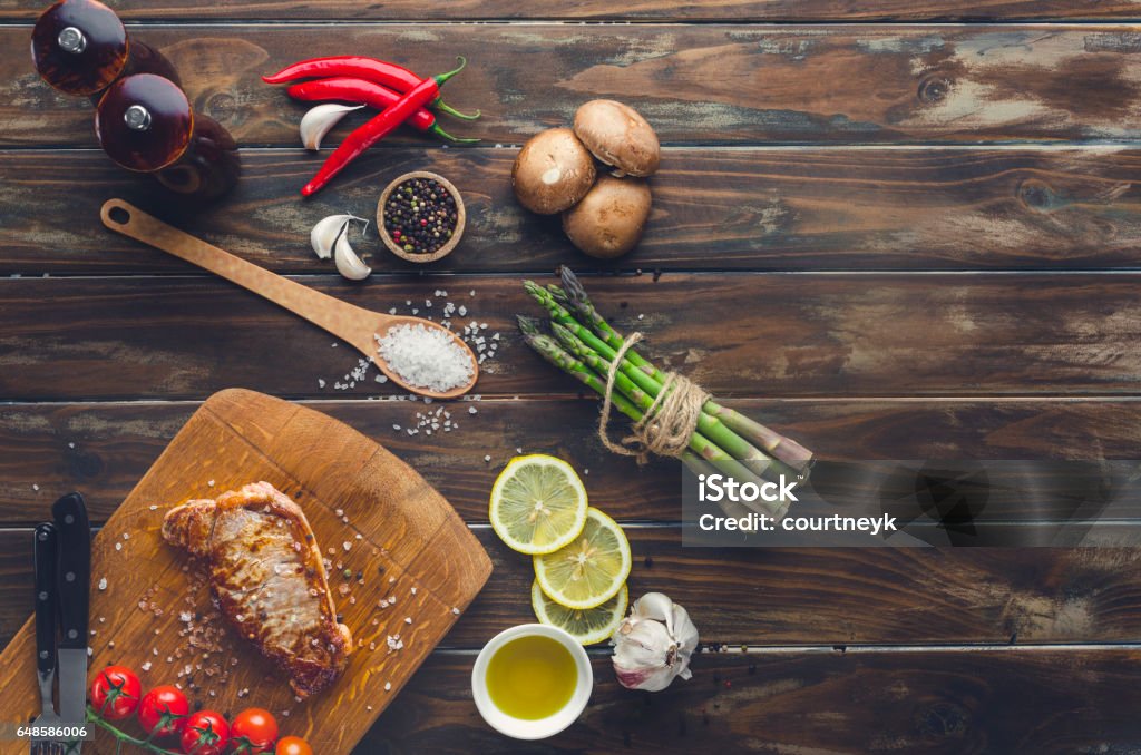 Cooked steak on a cutting board. Cooked steak on a cutting board. There are also cherry tomatoes and asparagus along with lemon; chilli; salt pepper and cutlery. Ingredient Stock Photo