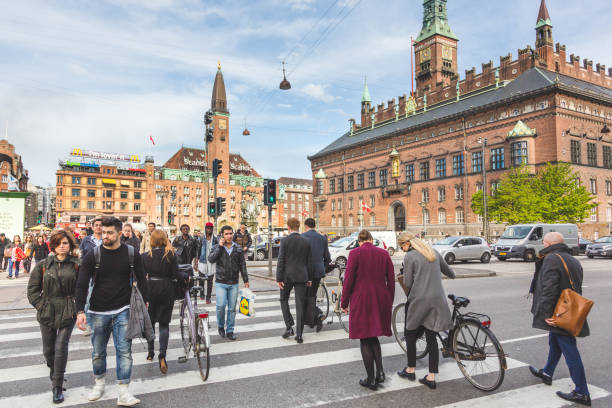 People crossing on zebra in the city. Commuters and tourists walking and carrying bicycles. City hall on background