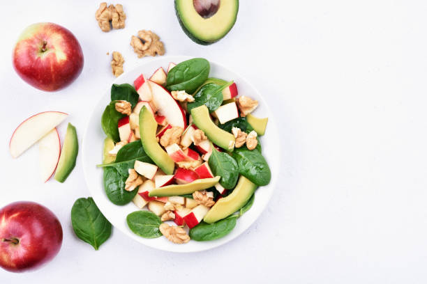 Healthy fruit salad Fruit salad with red apples, avocado, spinach and walnut on light background with copy space, top view green apple slice overhead stock pictures, royalty-free photos & images