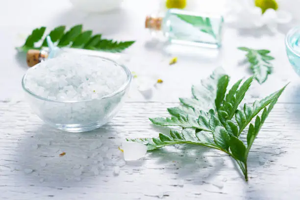 spa setting with bath salt and fern leaves on white wooden table background