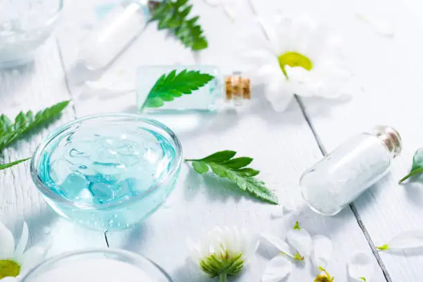 spa setting with cosmetic cream, gel, bath salt and fern leaves on white wooden table background