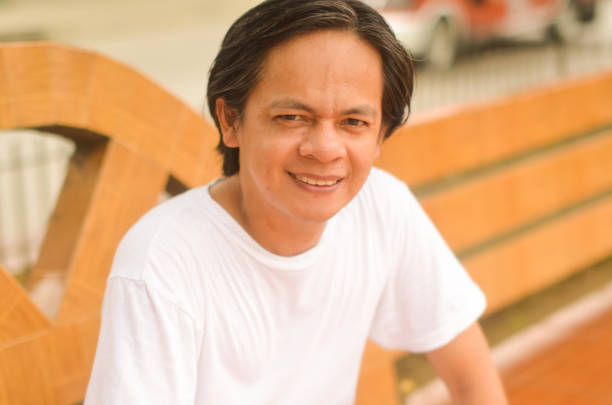 Photograph image of an Asian man with big nose, smiling, sitting at the park.