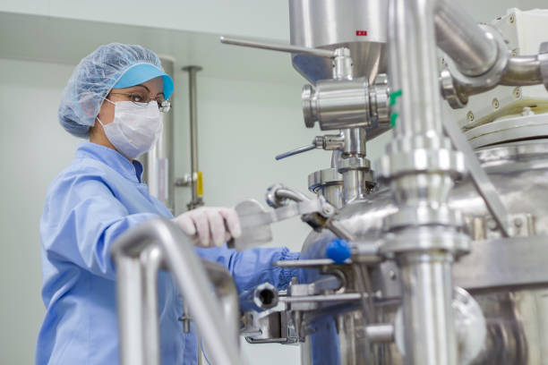 Portrait of Pharmaceutical Worker - Sterile Environment Preparing machine for work in pharmaceutical factory. Female worker wearing protective clothing in pharmaceutical plant. pharmaceutical factory photos stock pictures, royalty-free photos & images