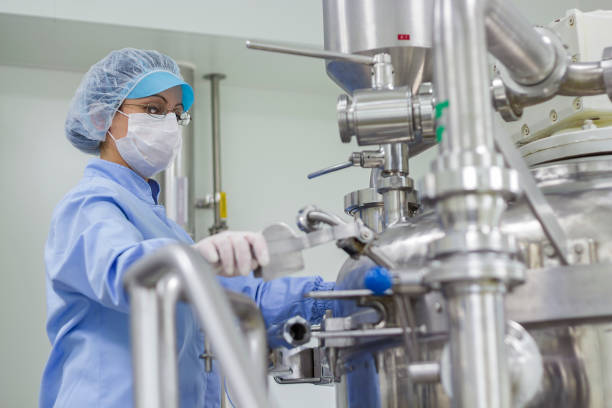 Portrait of Pharmaceutical Worker - Sterile Environment Preparing machine for work in pharmaceutical factory. Female worker wearing protective clothing in pharmaceutical plant. pharmaceutical manufacturing machine stock pictures, royalty-free photos & images