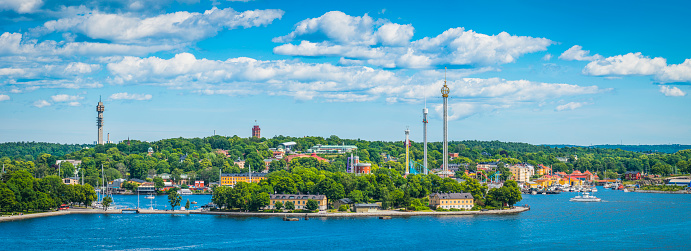 Panoramic view over the blue waters of Stockholm's inner harbour to the green islands of Skeppsholmen and Djurgarden, the towers of Grona Lund and Kaknastornet and the colourful waterfront villas of Sweden's vibrant capital city.