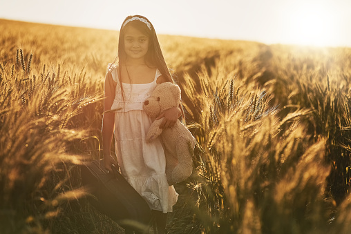 Portrait of a cute little girl playing with her teddybear in a cornfield