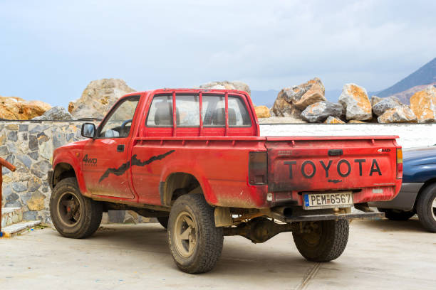 Old red pickup truck Toyota parked on Mithos beach promenade in sea Harbour of resort village Bali. Light 4wd truck Japanese production. Rethymno, Crete, Greece