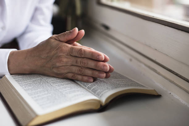 istock Old woman praying with bible open in front of her 648768896