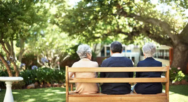 Rearview shot of a group of seniors sitting together on a bench out in the garden