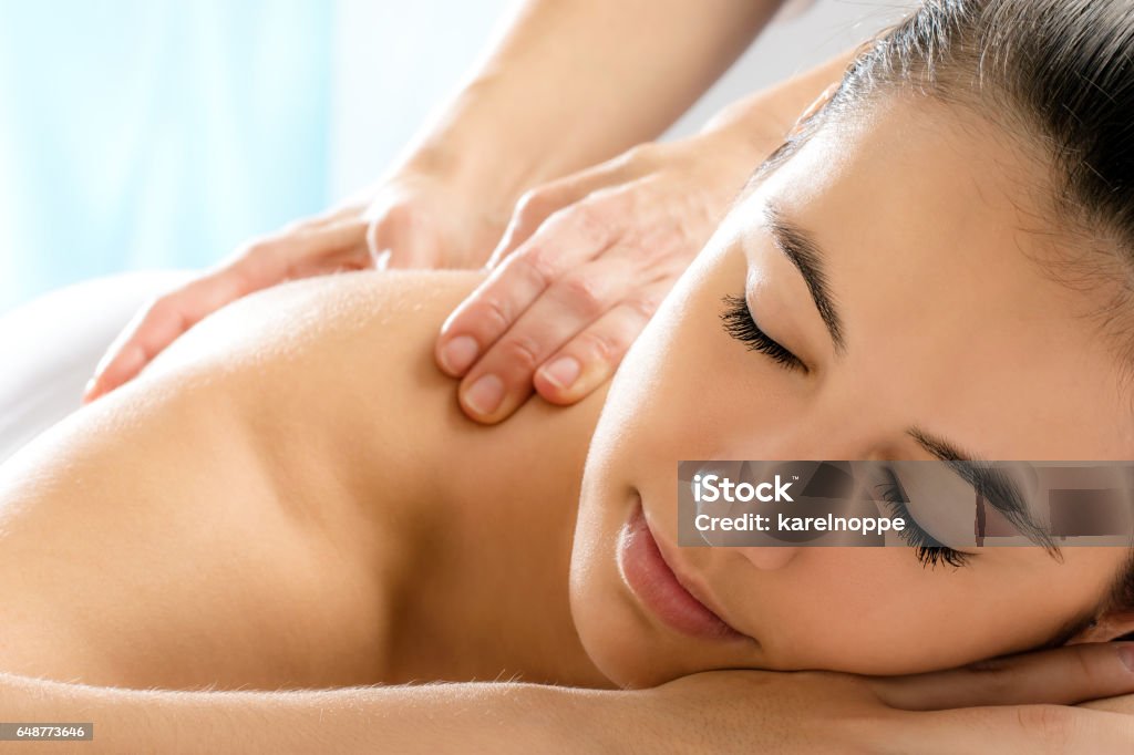 Woman with relaxing face expression in spa. Close up portrait of young woman relaxing in spa.Therapist doing back massage on girl in background. Massaging Stock Photo