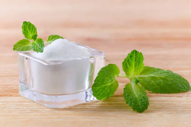 Photo of birch sugar xylitol in a glass bowl with mint on wooden closeup