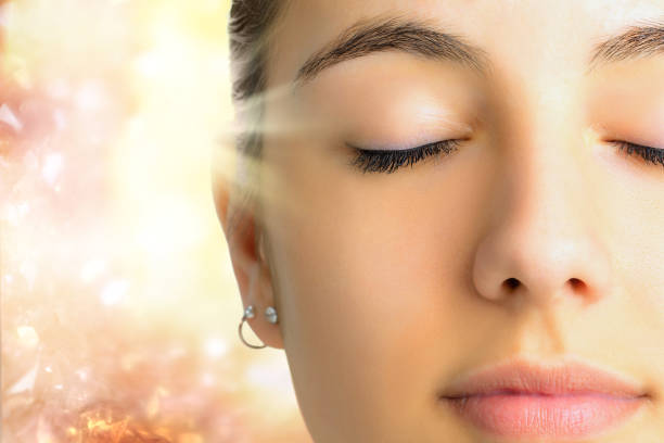 Relaxed face shot of woman meditating. Extreme Close up face shot of young woman with eyes closed.Girl doing mental exercise against bright background with light beam. spiritual enlightenment stock pictures, royalty-free photos & images