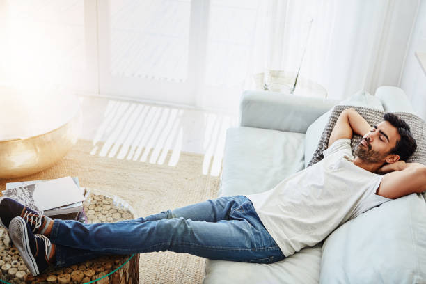 Now for some rest and relaxation Shot of a man relaxing on the sofa at home laziness photos stock pictures, royalty-free photos & images