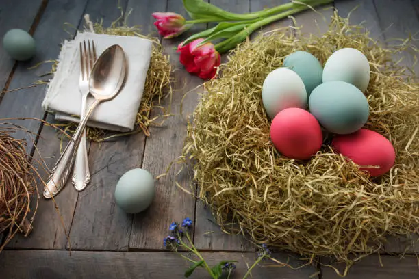 Decoration with colorful easter eggs in a nest and flowers on a old shabby wooden table