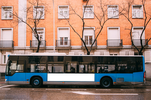 A blue bus at a street, with a blank billboard.