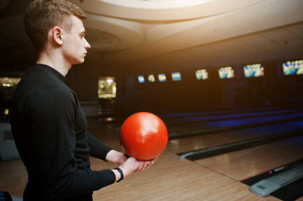 istock Young man holding a bowling ball standing against bowling alleys with ultraviolet light. 648821332