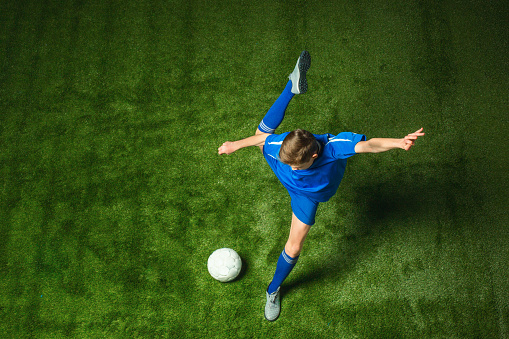 Young boy with soccer ball doing flying kick, on green studio background