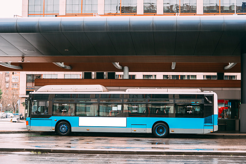 A blue bus at a street, with a blank billboard.