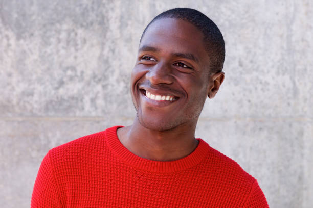 sonriente a hombre afroamericano en suéter rojo mirando lejos - cardigan men african ethnicity african descent fotografías e imágenes de stock