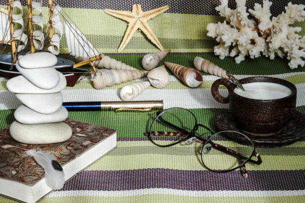 Notepad and glasses, Cup of coffee on the table with pebbles from the sea, the sea green background