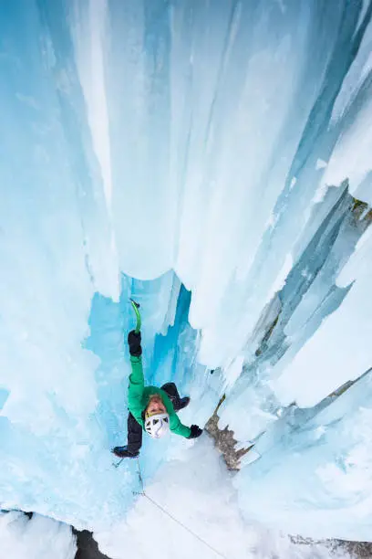 High angle view of man ice climbing on frozen waterfall with blue icicles